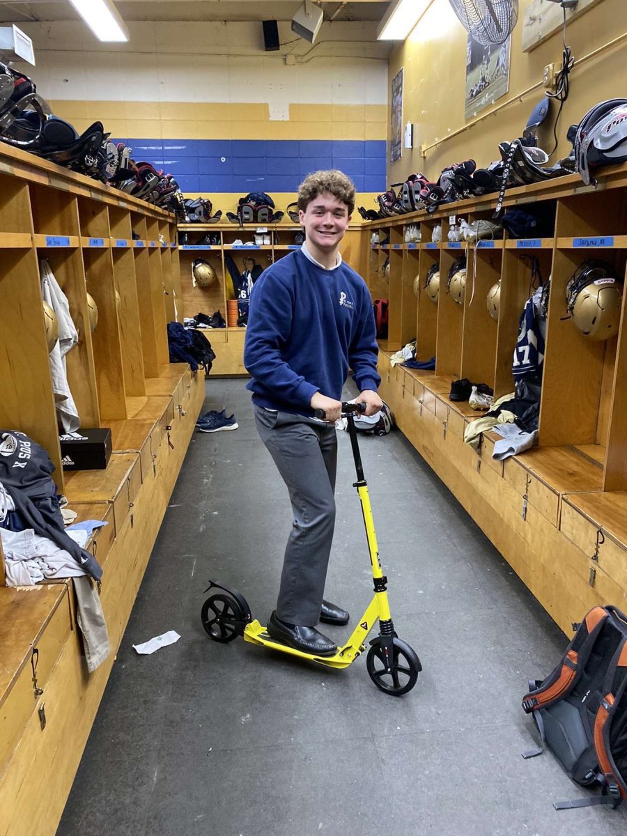 Junior football player Colin Crosby rides on his scooter in the locker room. After their parking spots were moved across the street, Crosby and several of his junior teammates started using scooters to get to weightlifting in the morning. Staff photo.