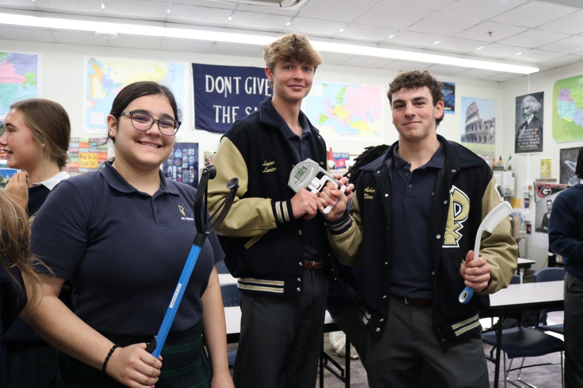 Juniors Maria Jose Serafin-Moreno, Logan Lanier, and Asher Klein hold adaptive tools commonly used in pediatric occupational therapy to help children complete everyday activities. This was one of more than 35 careers represented at the annual Career Day, where juniors and seniors attended brief presentations from guest speakers across a wide range of fields. 
